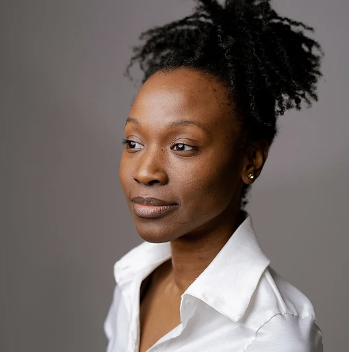 Black woman in a white dress shirt looking away from the camera with light shining on her face.